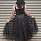 Person wearing a black dress with sheer overlay in front of a corrugated metal wall.