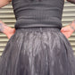 Person wearing a black tank top and tulle skirt with tattoos on arms and back.