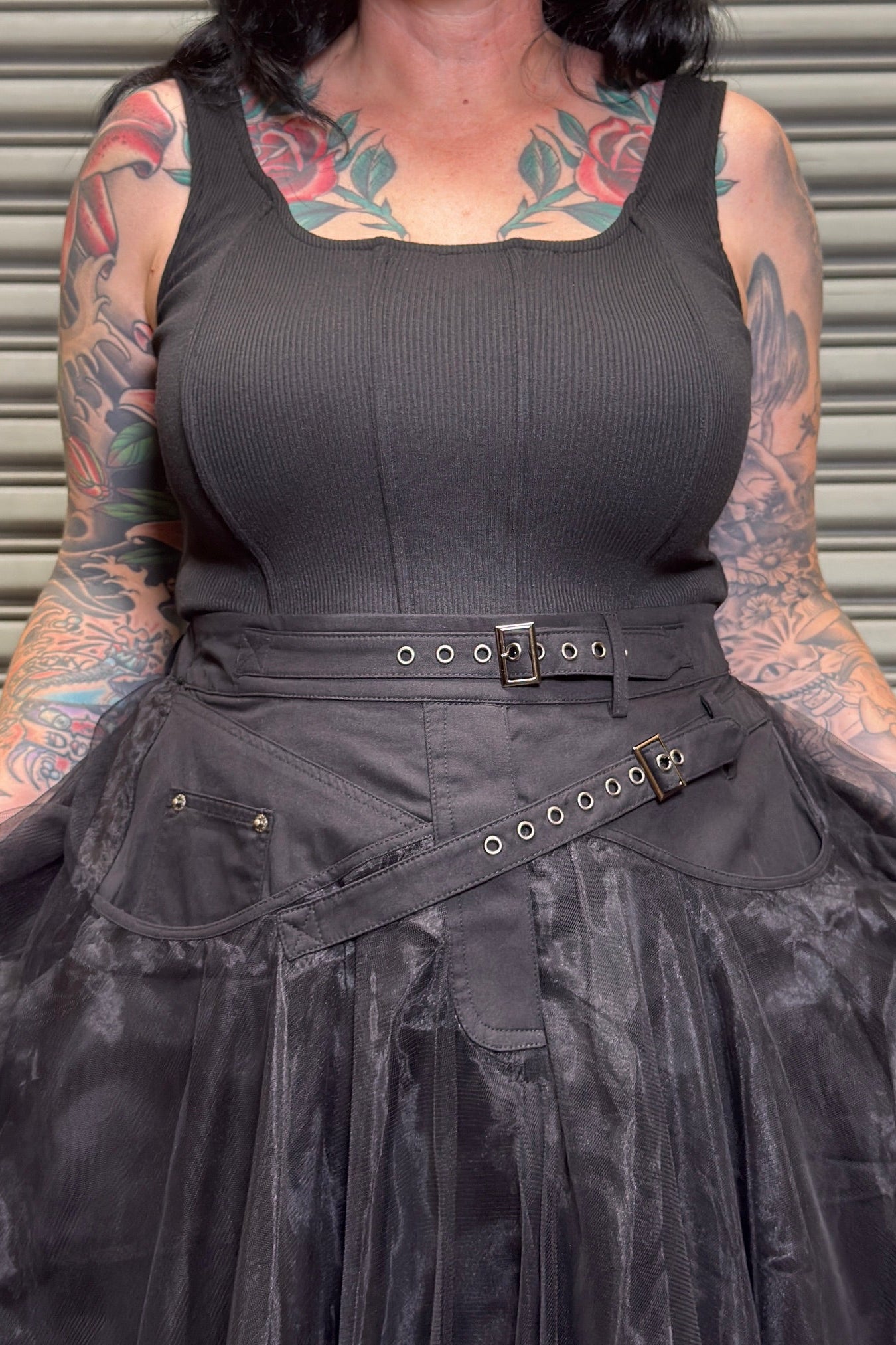 Person wearing a black sleeveless top and skirt with tattoos on arms and neck.