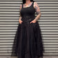 Person wearing a black dress with a tattooed arm standing in front of a metal shutter.