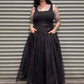 Woman wearing a black sleeveless top and long black skirt standing in front of a corrugated metal wall.