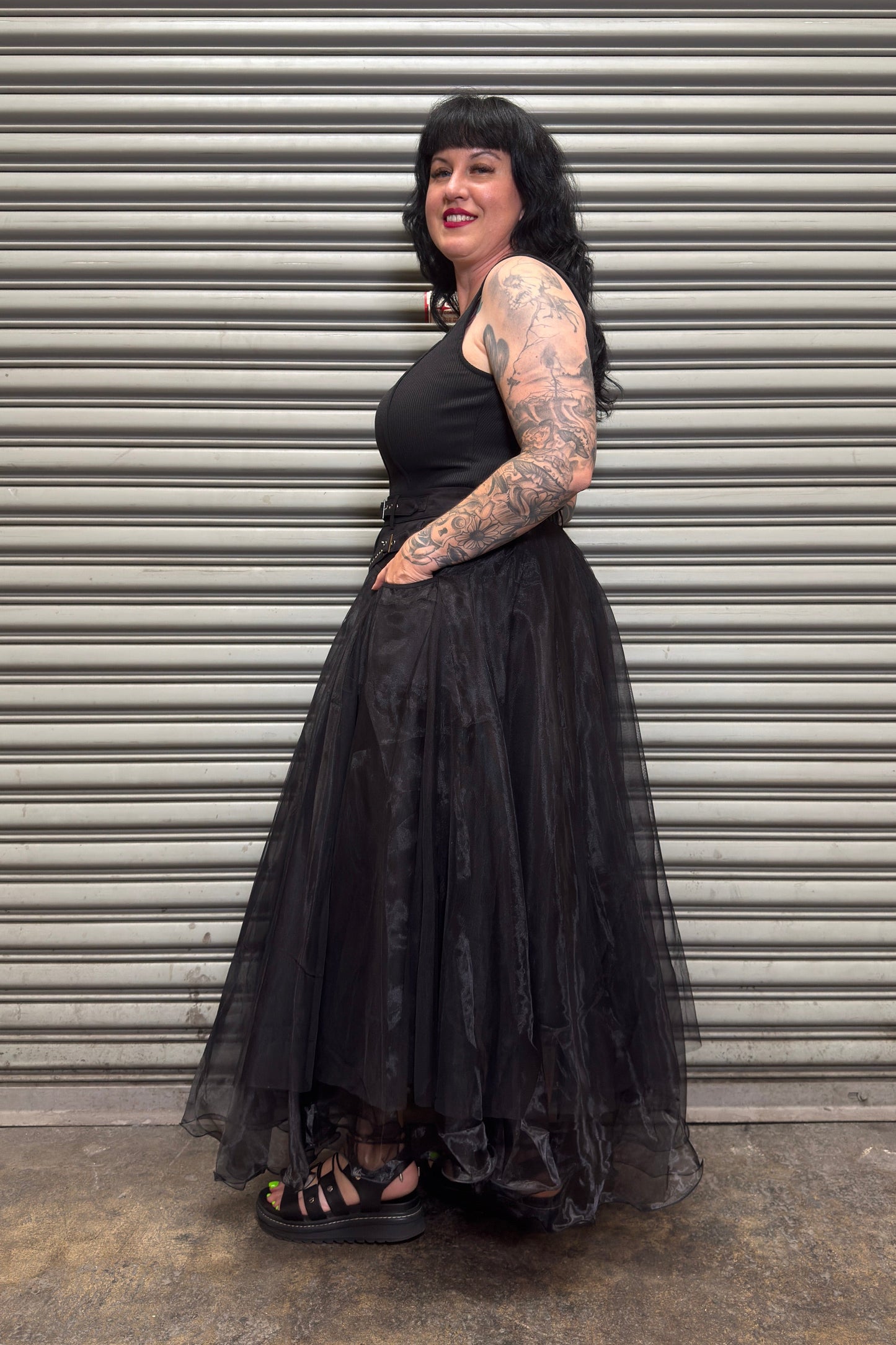 Woman wearing a black dress standing in front of a metal shutter.
