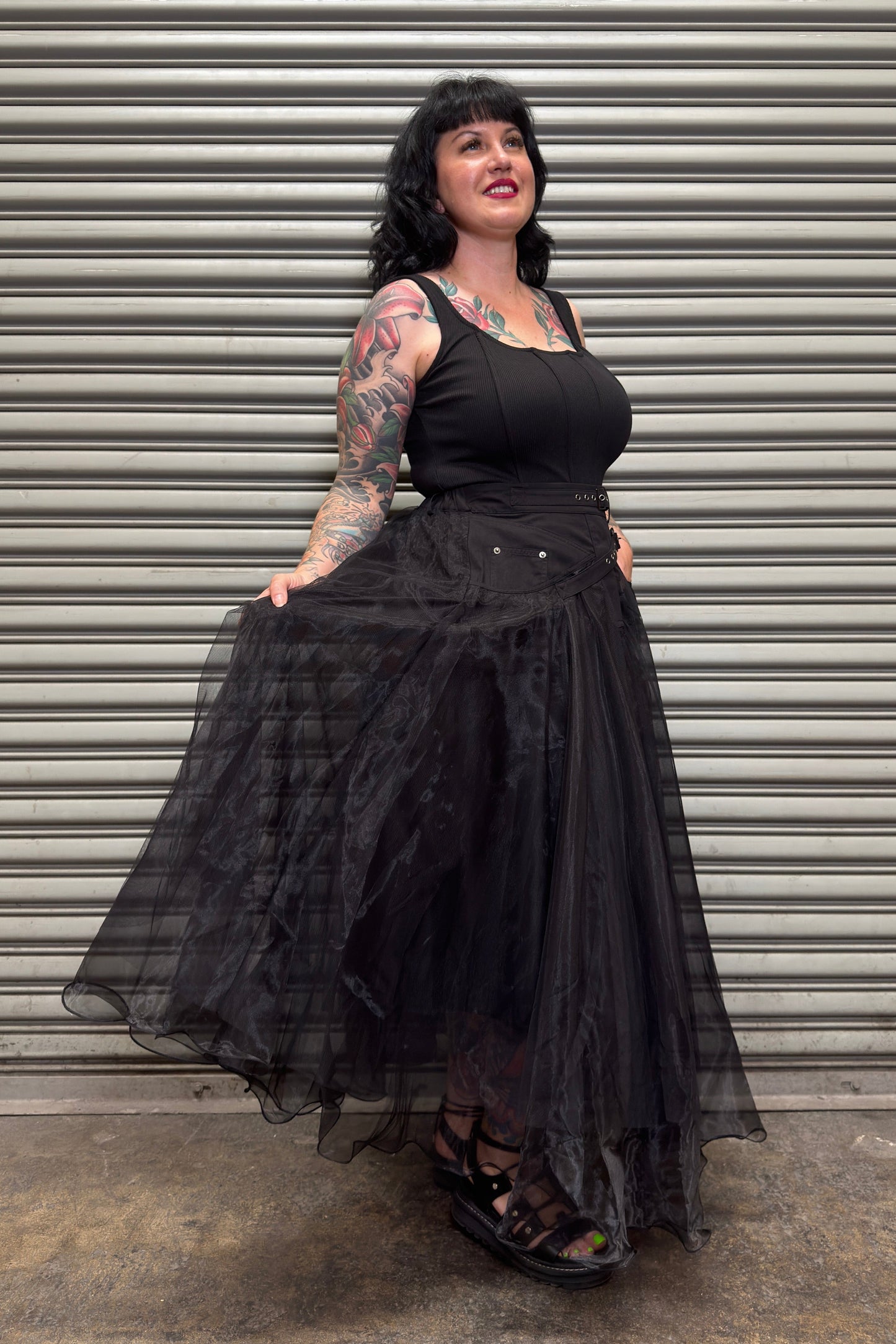 Woman wearing a black dress with sheer sleeves against a metal shutter background