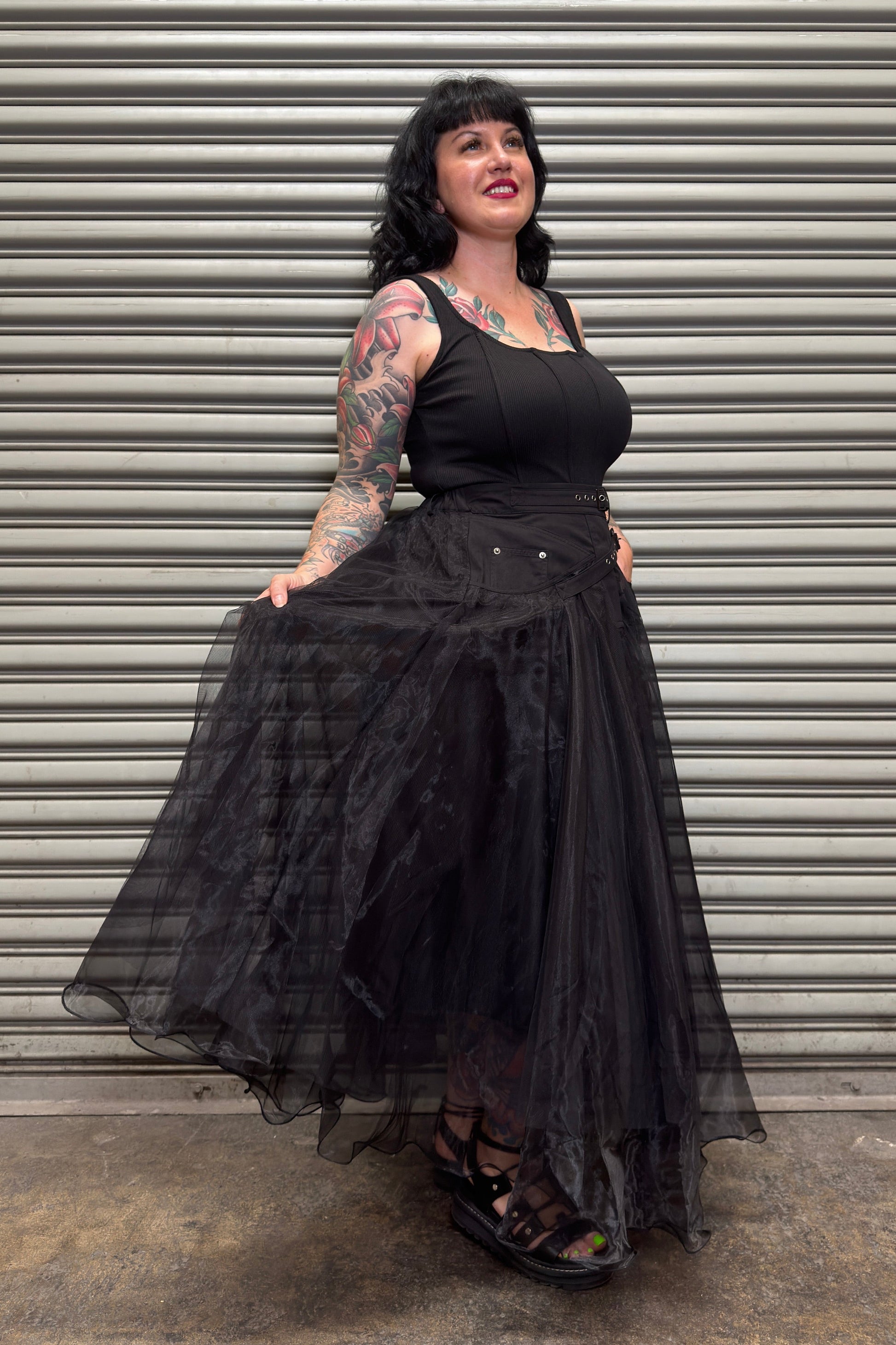 Woman wearing a black dress with sheer sleeves against a metal shutter background