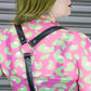 Person wearing a pink and green patterned leopard dress with a black harness over a gray background