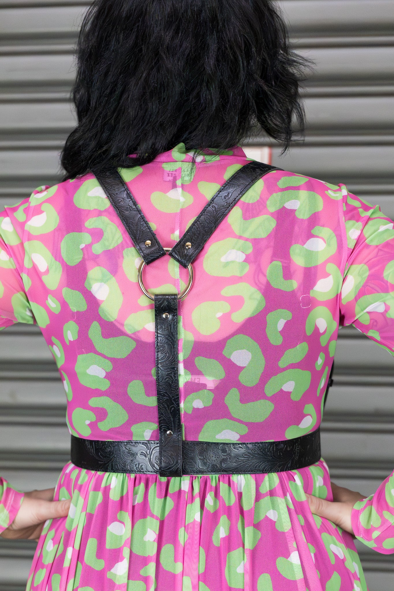 Person wearing a pink and green patterned dress with black harness.