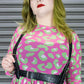 Person wearing a pink dress with green leopard pattern and a harness against a metallic background