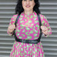 Woman wearing a pink dress with leopard green pattern and a black harness against a metallic background