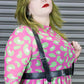 Woman wearing a pink dress with green leopard patterns and a black harness against a metallic background