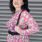 Woman wearing a pink and green patterned dress with a harness against a metallic background