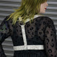 Person wearing a black dress with leopard print and a white harness against a metallic background