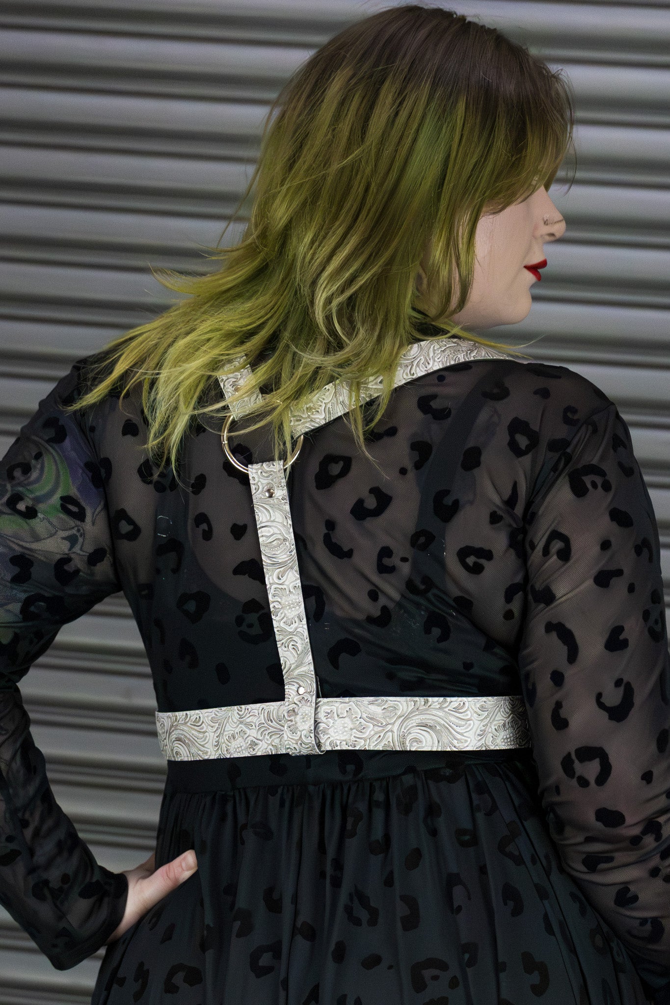 Person wearing a black dress with leopard print and a white harness against a metallic background