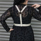 Person wearing a black dress with a leopard print pattern and a white harness against a metallic background.