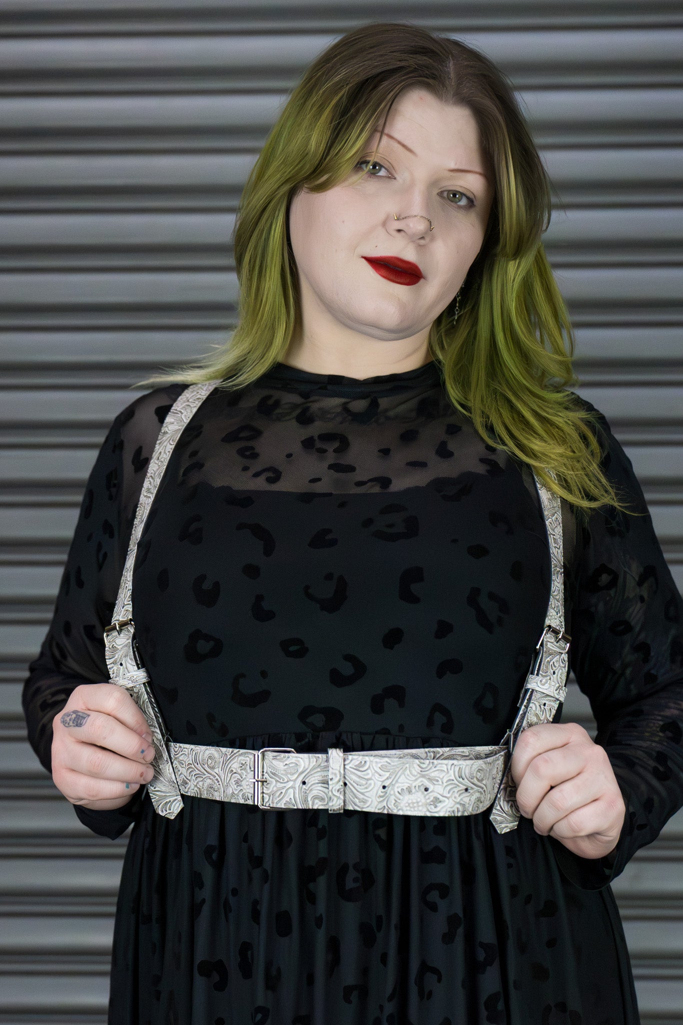 Person wearing a black dress with a sheer top and white harness against a metallic background
