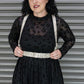 Woman wearing a black dress with a sheer overlay and white harness against a metallic background