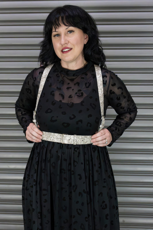 Woman wearing a black dress with a sheer overlay and white harness against a metallic background