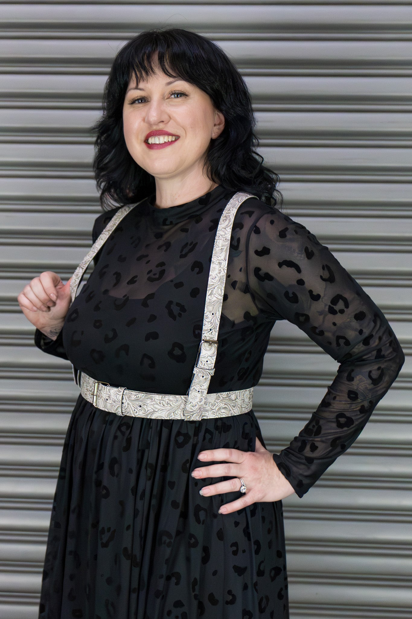 Woman wearing a black dress with a leopard print pattern and white harness against a metallic background.