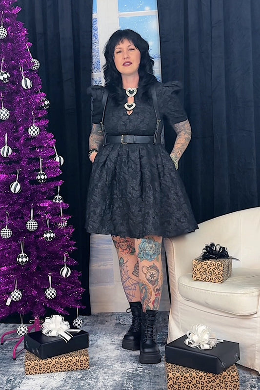 Woman in a black dress standing next to a purple Christmas tree with decorations.