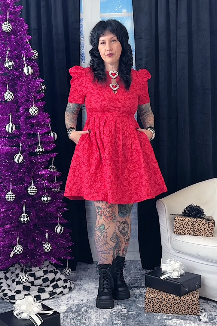 Person in a red dress standing next to a purple Christmas tree with decorations.