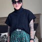 Person wearing a black turtleneck and green patterned pants in a bedroom setting