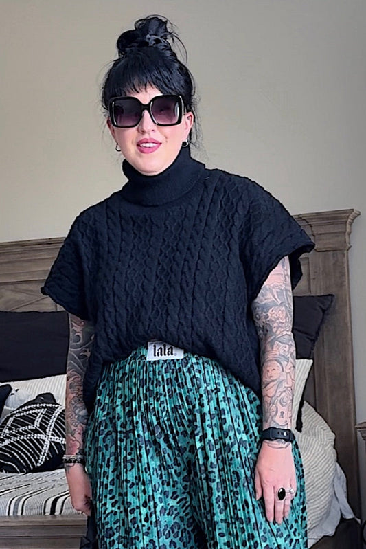 Person wearing a black turtleneck and green patterned pants in a bedroom setting