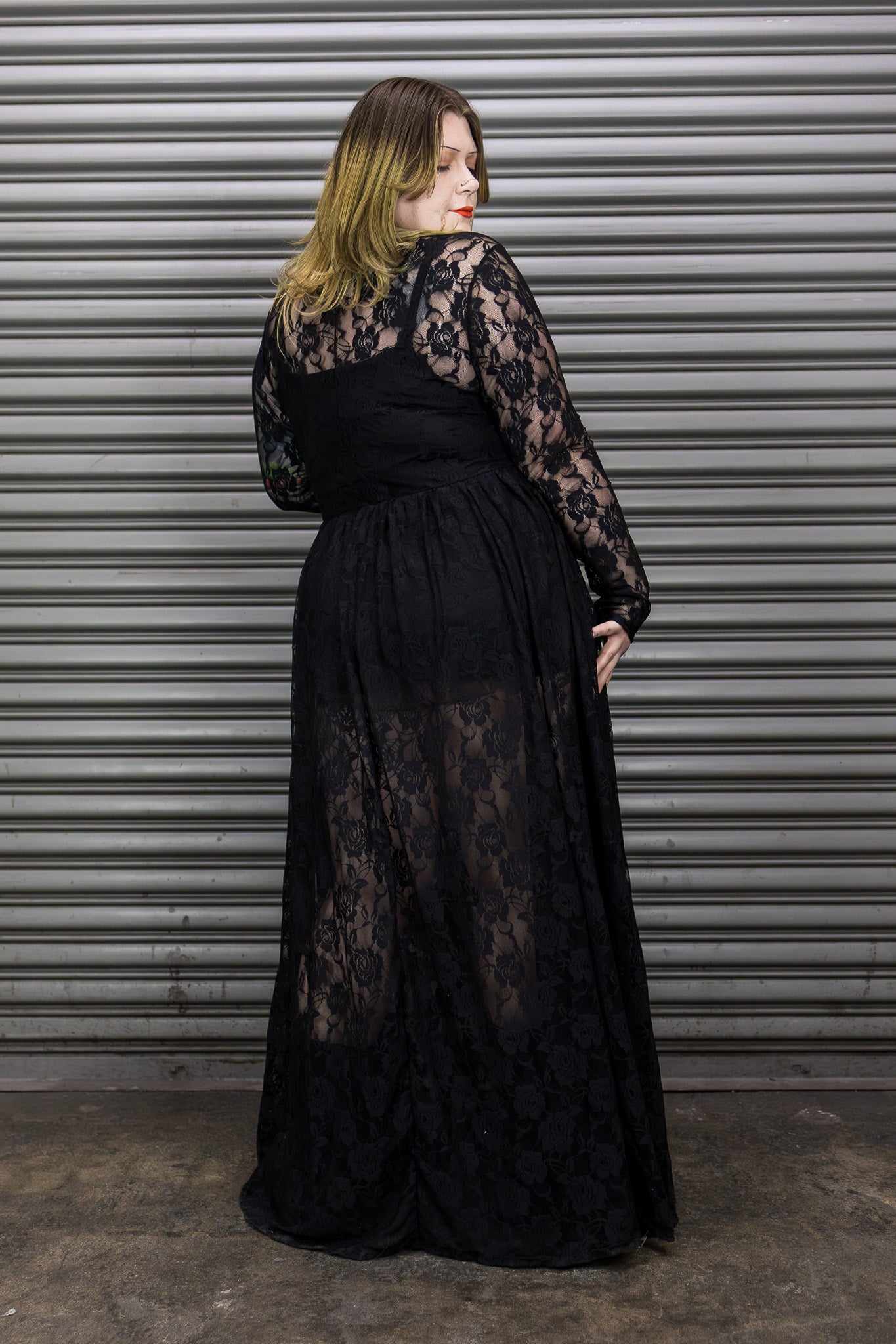 Woman wearing a black lace dress standing against a metallic shutter.