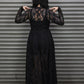 Person wearing a long black lace dress standing in front of a gray metal shutter.