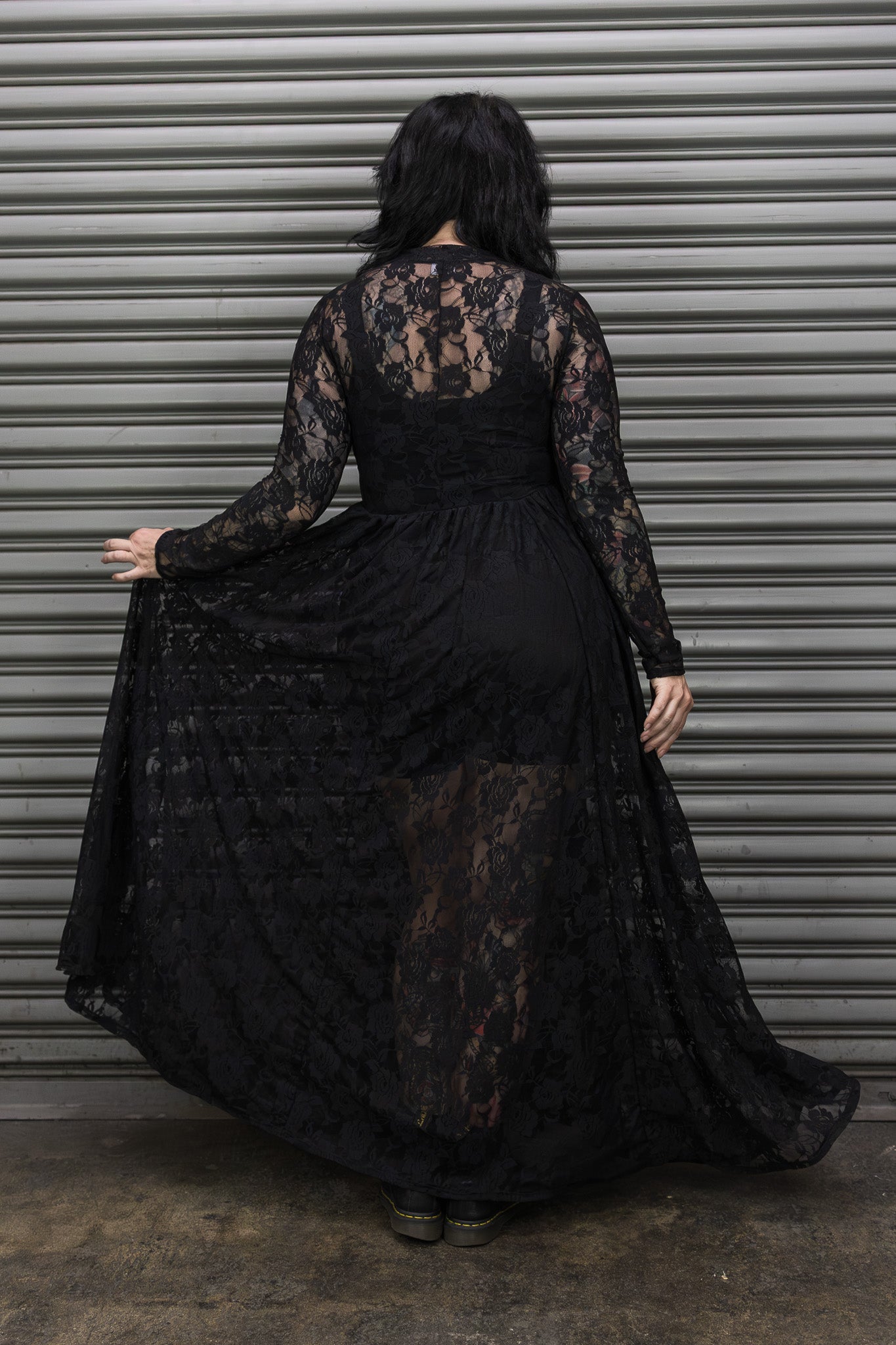 Person wearing a black lace dress standing in front of a metal shutter.
