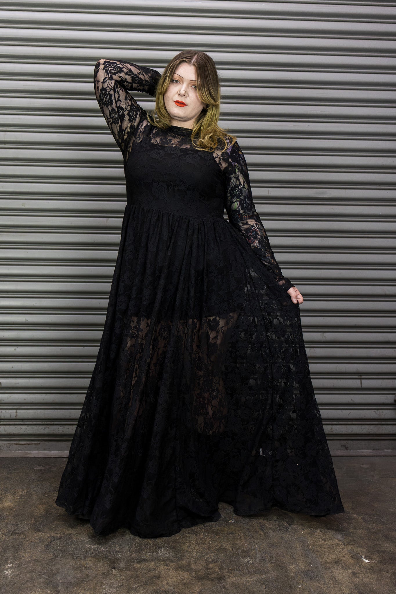 Person wearing a black lace dress against a metal shutter background.