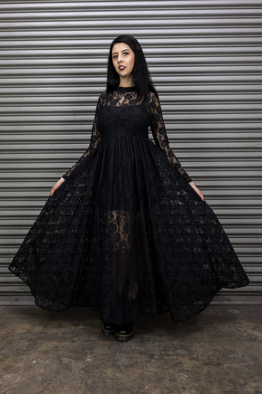 Woman wearing a black lace dress standing in front of a metal shutter.