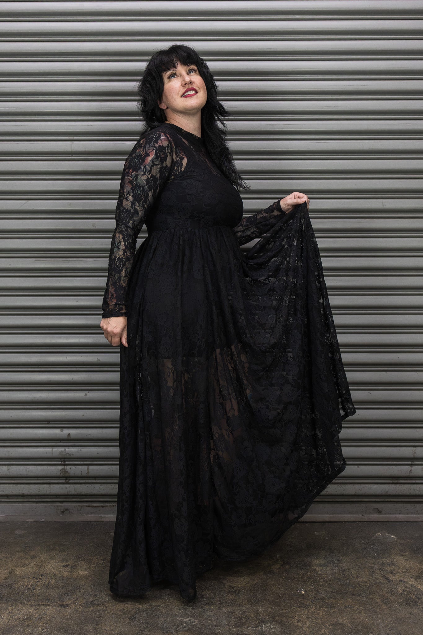 Person wearing a long black lace dress against a metal shutter background.