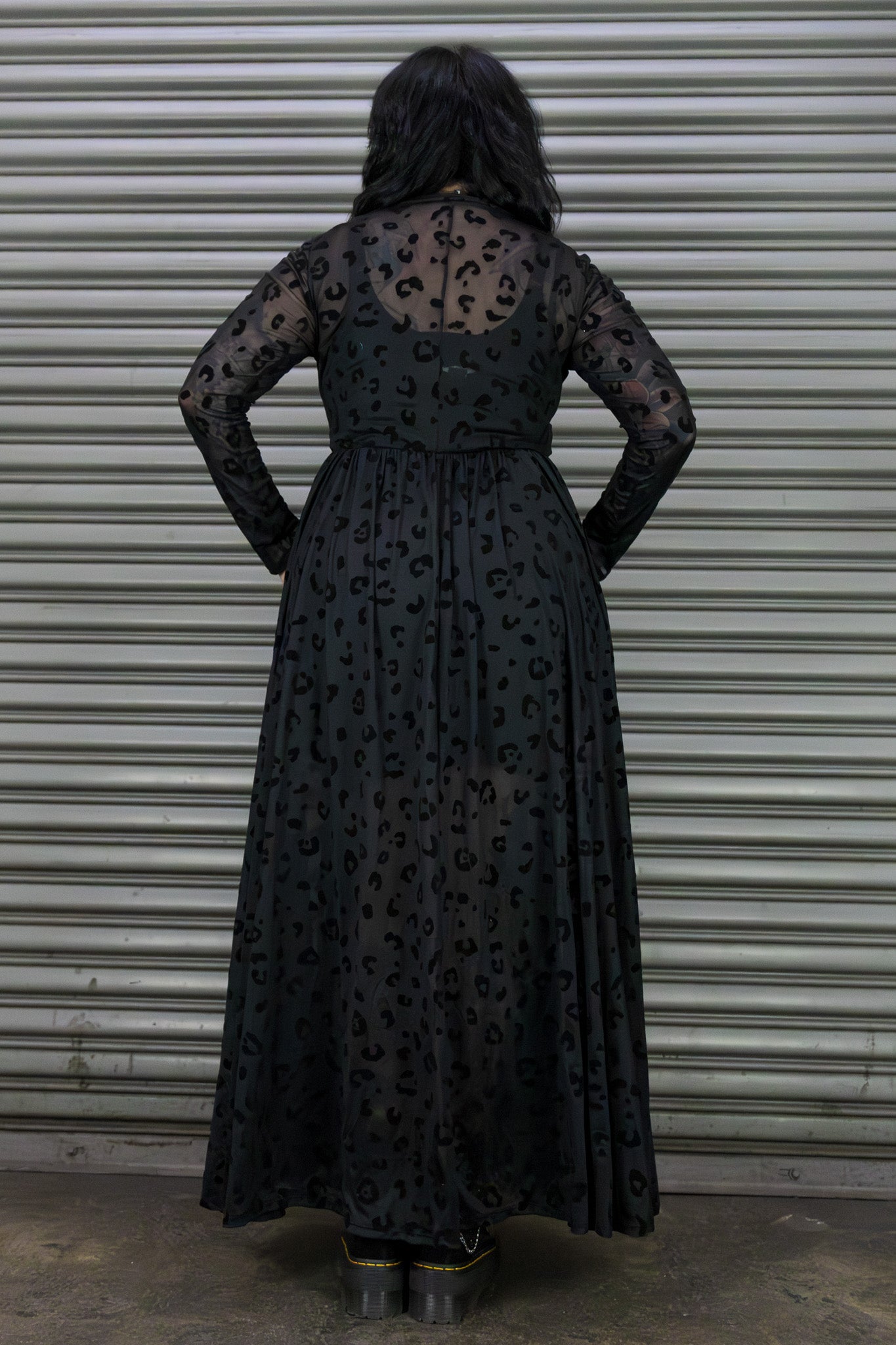 Person wearing a black dress with a leopard print pattern against a metal shutter background