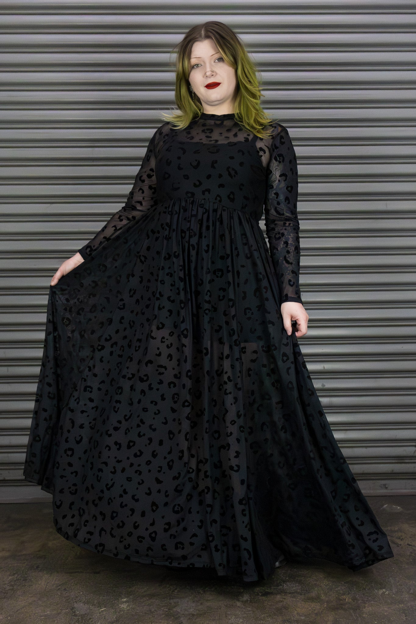 Person wearing a black dress with long sleeves and a pattern against a metallic background