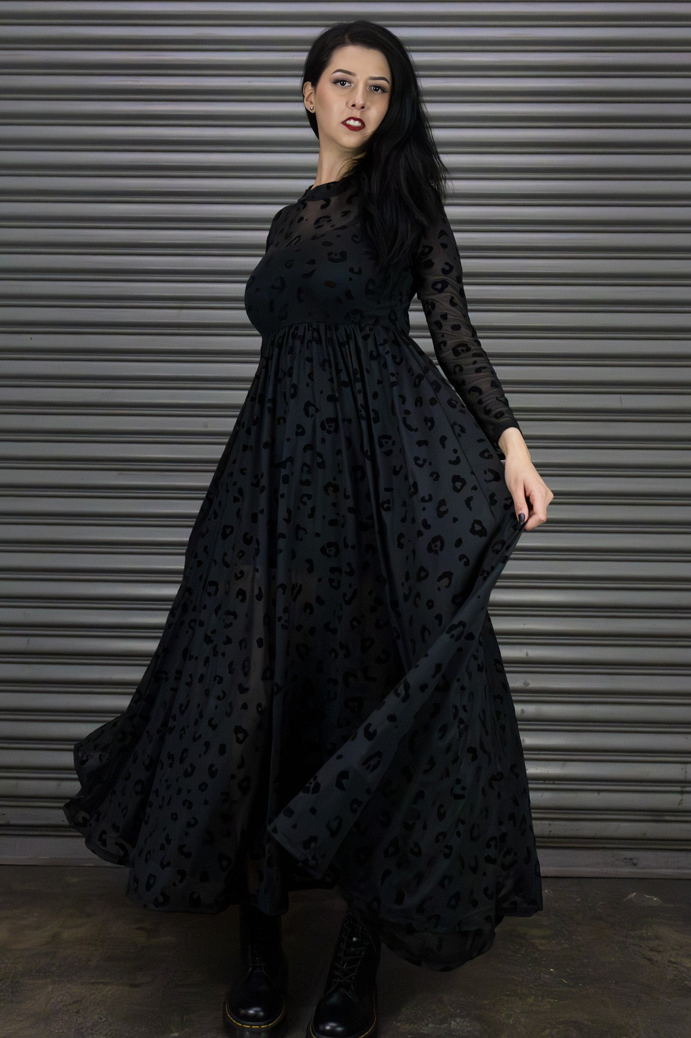 Woman wearing a black dress with a pattern in front of a metallic shutter.
