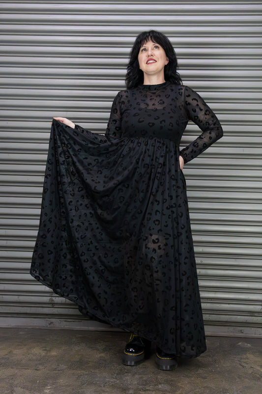 Woman wearing a black mesh leopard dress standing against a metal shutter.