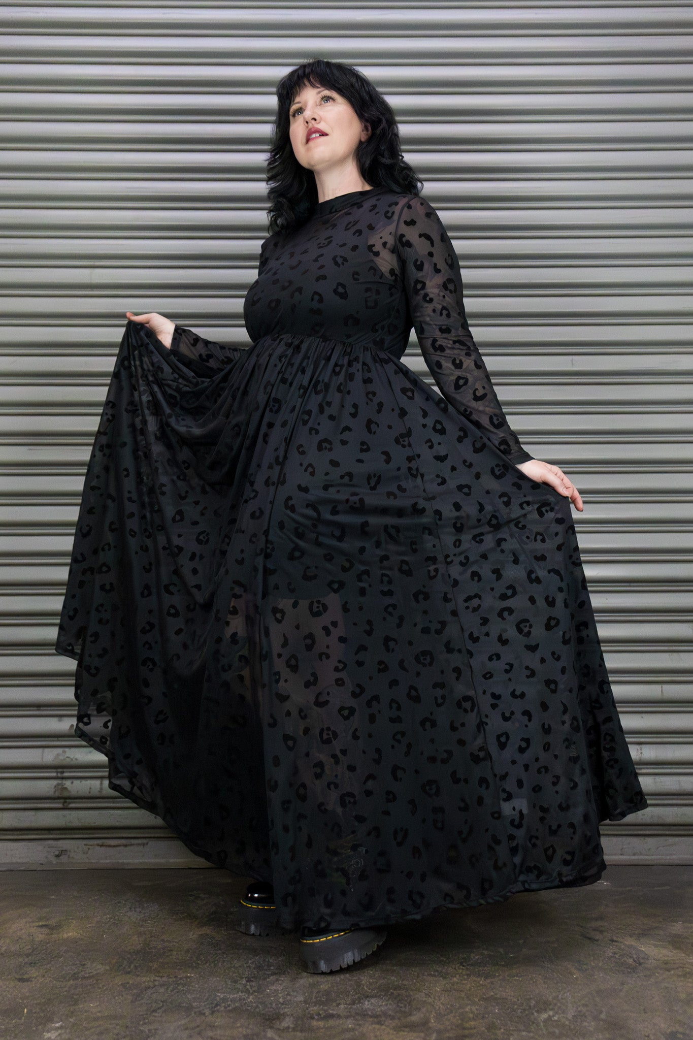 Woman wearing a black dress with a pattern in front of a metallic shutter.