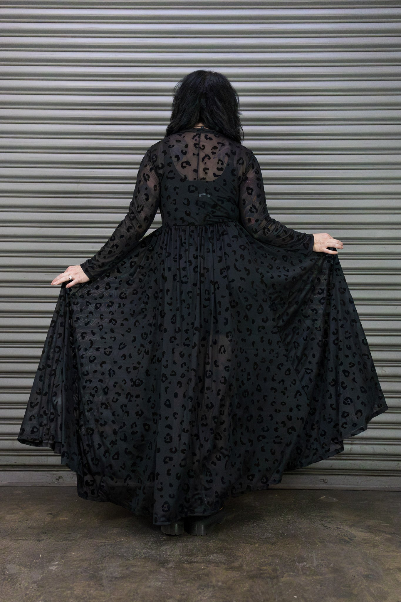 Person wearing a black dress with a pattern, standing in front of a metallic shutter.