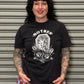 Person wearing a black t-shirt with graphic design and red and blue checkered shorts standing in front of a metallic shutter.