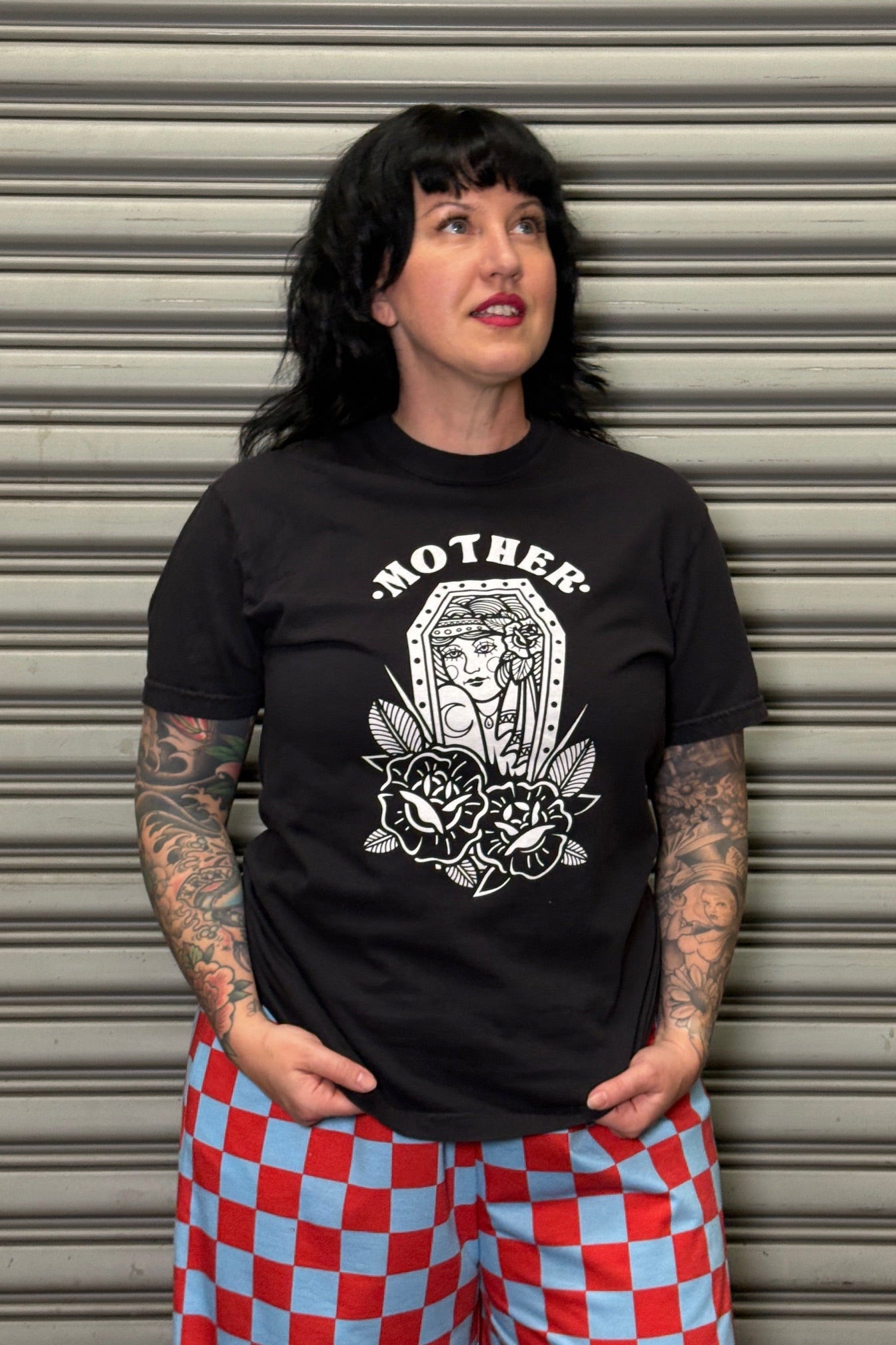 Person wearing a black t-shirt with a graphic design standing in front of a metallic shutter.