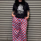 Person wearing a black t-shirt with a graphic design and red and blue checkered pants standing against a metal shutter.