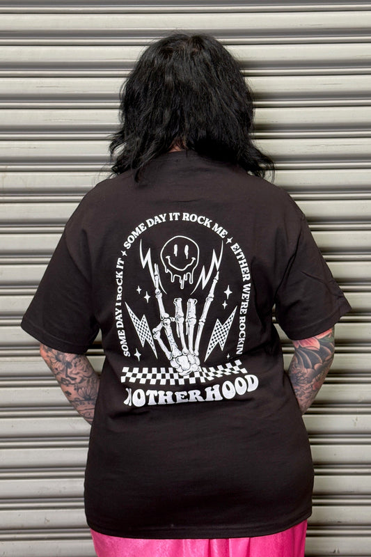 Person wearing a black t-shirt with a graphic design and text on the back, standing in front of a closed metal shutter.