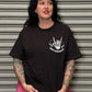 Person wearing a black t-shirt with a white graphic design in front of a metallic shutter.