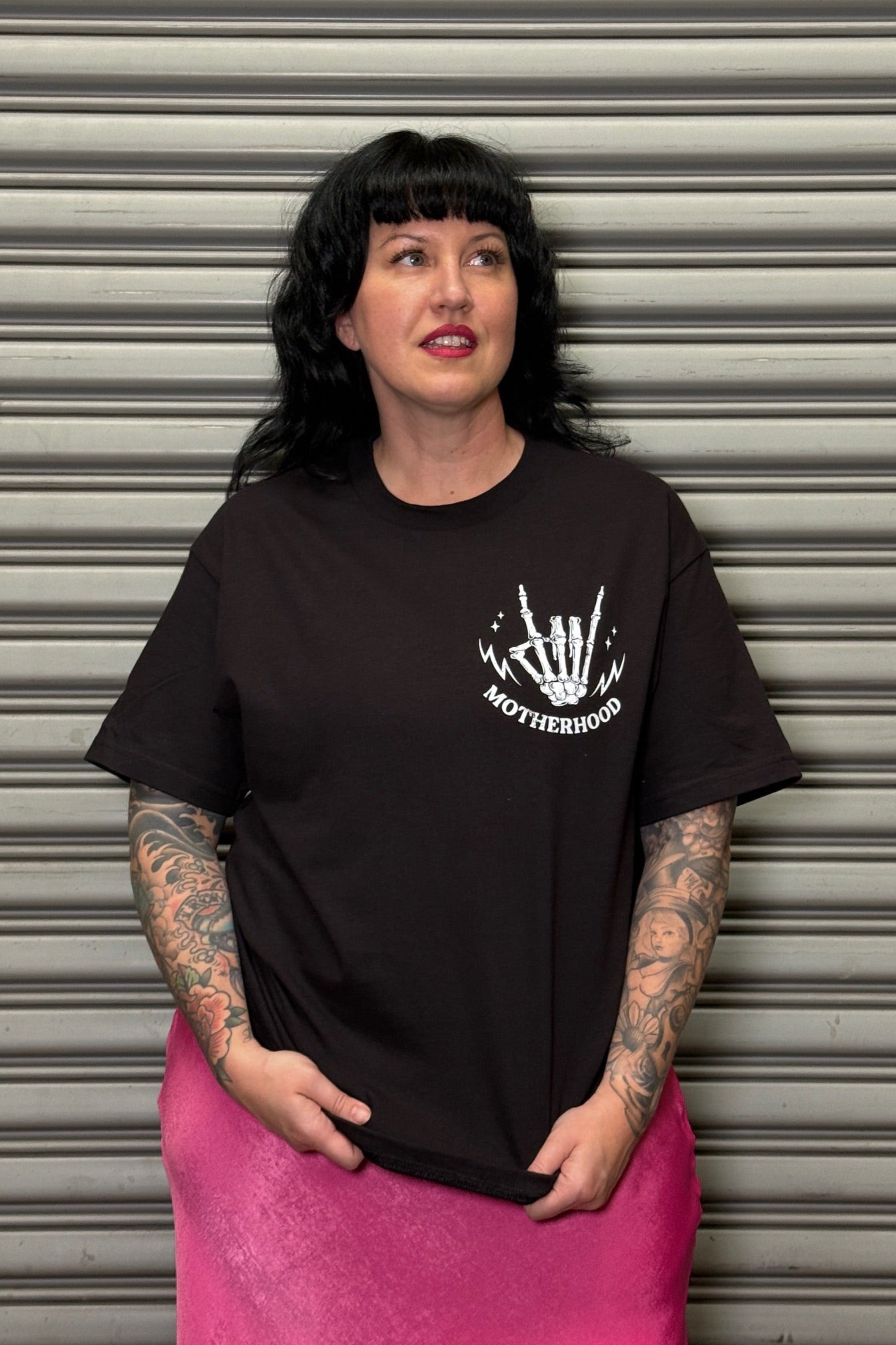 Person wearing a black t-shirt with a white graphic design in front of a metallic shutter.