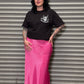 Person wearing a black t-shirt and pink skirt standing in front of a metal shutter.