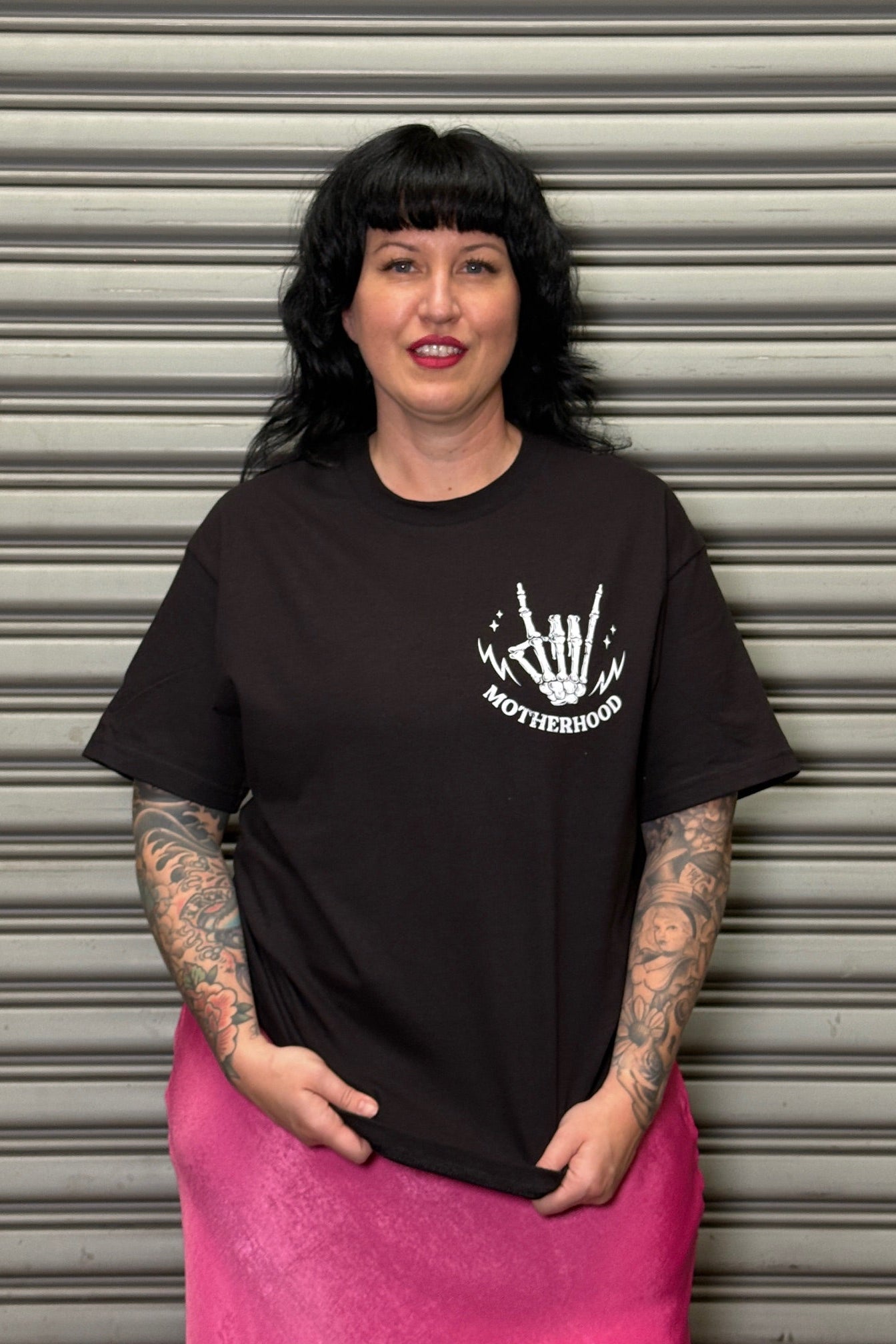 Woman wearing a black t-shirt with a white graphic design in front of a metallic shutter.