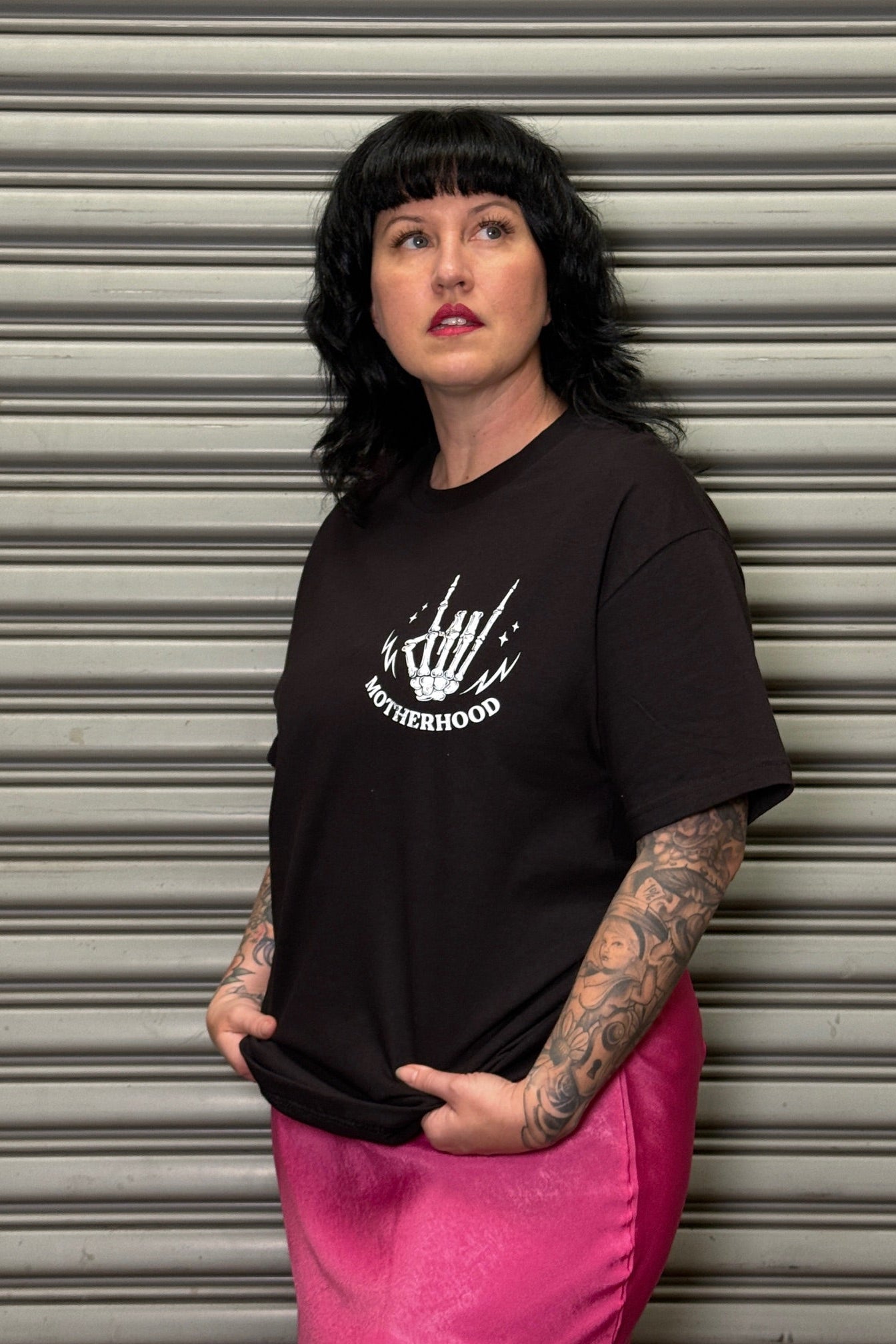 Woman wearing a black t-shirt with a graphic design in front of a metallic shutter.