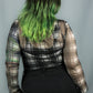 A person shown from the back wearing a sheer long-sleeve plaid top with black and white tones and bright green ombre hair, paired with black pants, against a plain gray background.