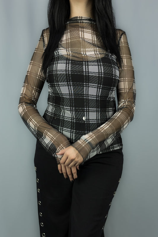 A woman wearing a sheer long-sleeve mesh top with a black and white plaid pattern over a black camisole, paired with black pants, set against a plain gray background.