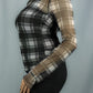 A woman wearing a sheer long-sleeve mesh top with a black and white plaid pattern, paired with black pants, shown from a side profile against a solid gray background.