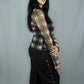 A woman modeling a long-sleeve sheer mesh top with a black and white plaid pattern, paired with black wide-leg pants featuring decorative buttons down the side, set against a plain gray studio backdrop.